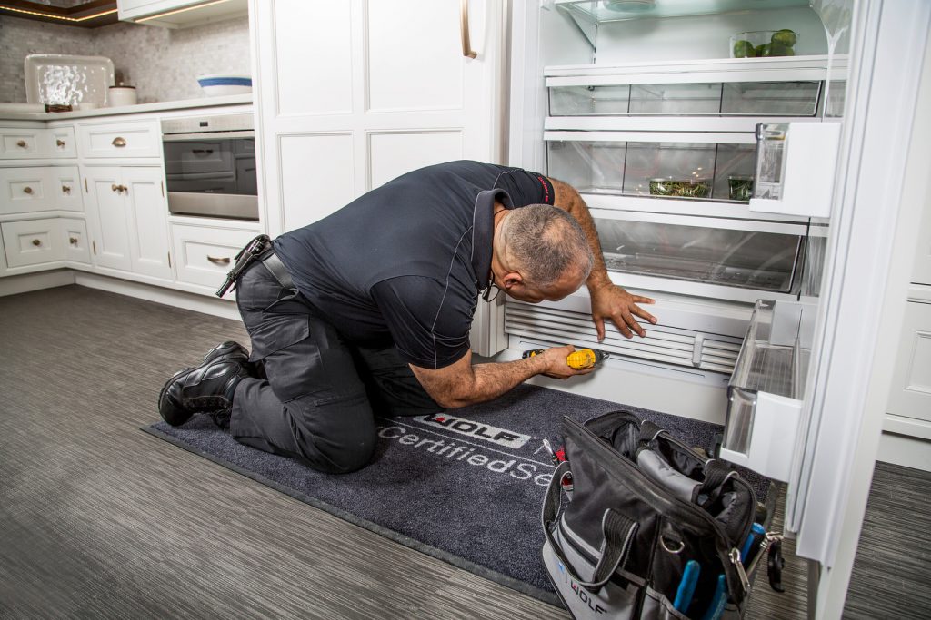 luxury appliance repair technician servicing a fridge in new england