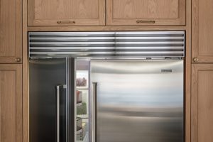 A Sub-Zero stainless steel refrigerator with double doors is built into wooden cabinetry; the left door is slightly open, revealing food items inside this premium kitchen appliance.