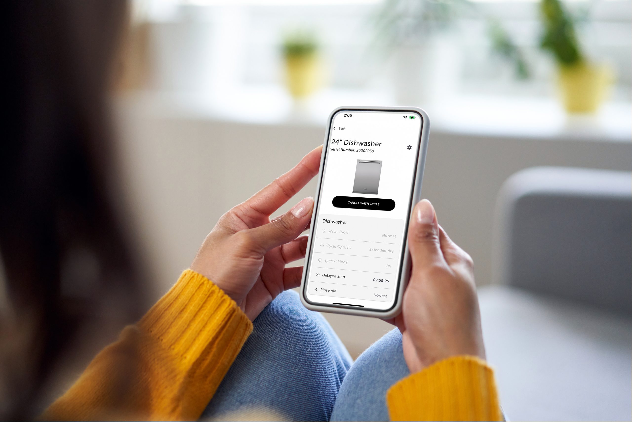 Person holding a smartphone displaying an appliance management app, showing details for a 24" Cove dishwasher.