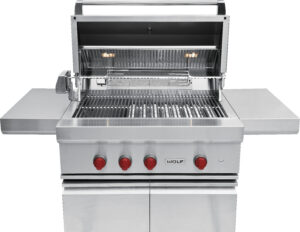 A stainless steel outdoor gas grill with four red control knobs, an open hood, side shelves, and internal lights.